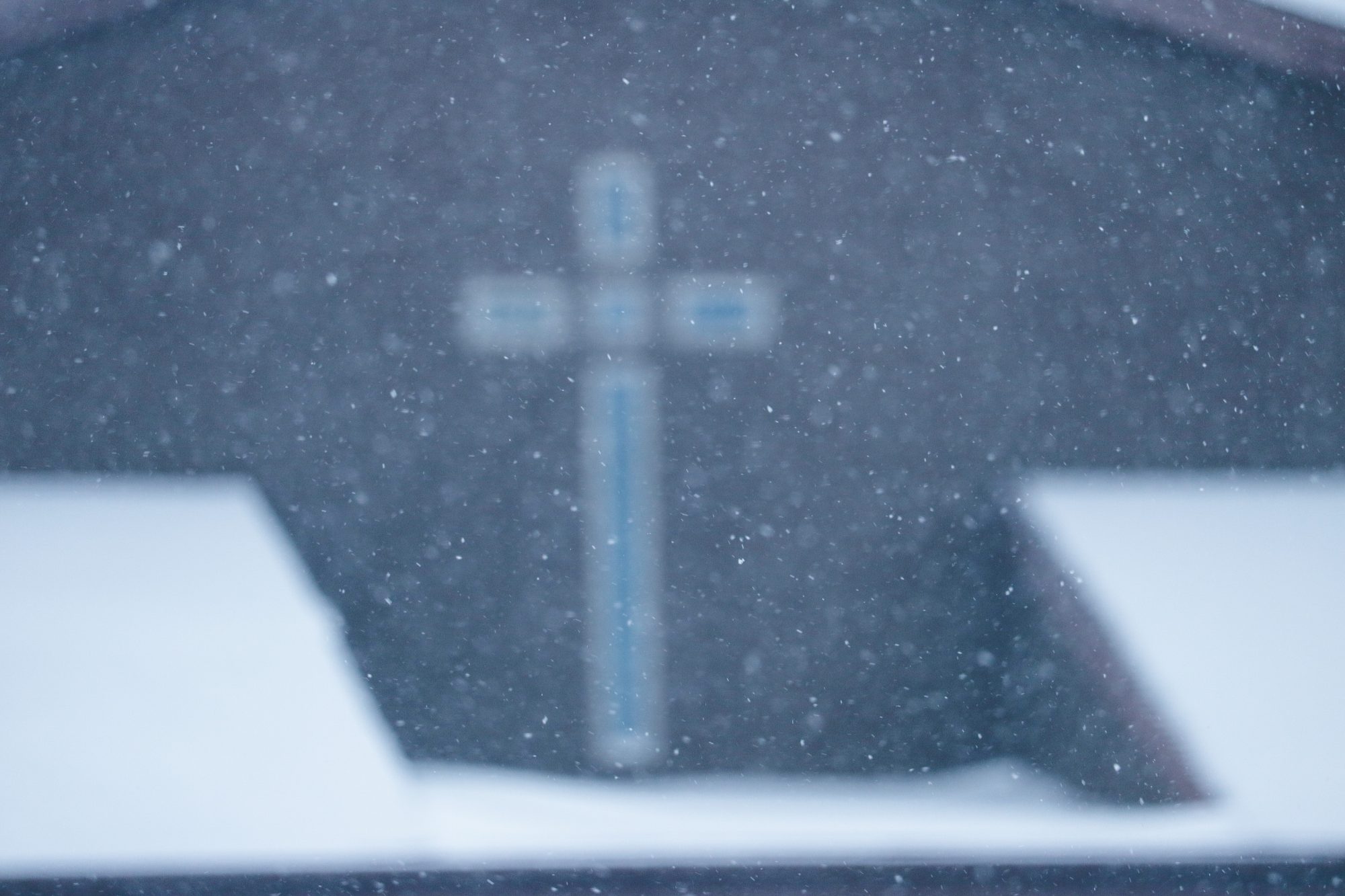 The image is of a white cross in the distance made blurry by the snowfall